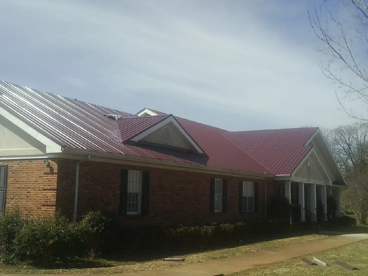 Red metal roof with gabled entries on a long brick building, from a Hail Damage Roof Repair job in Gibbsboro