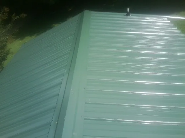 New green metal panels meeting at the ridge of a roof — Flat Roof Repair work by our crew in Gibbsboro