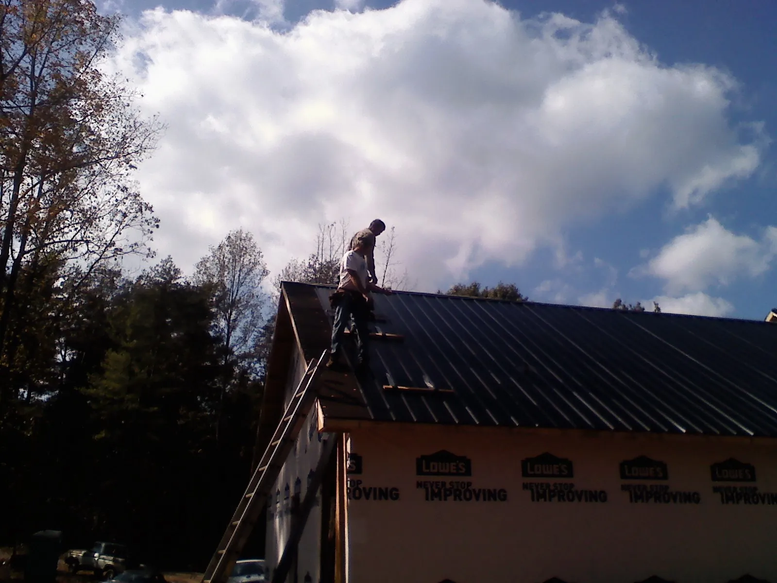 Roofer fastening dark metal panels high against a cloudy sky, from a Roof Inspection job in Gibbsboro